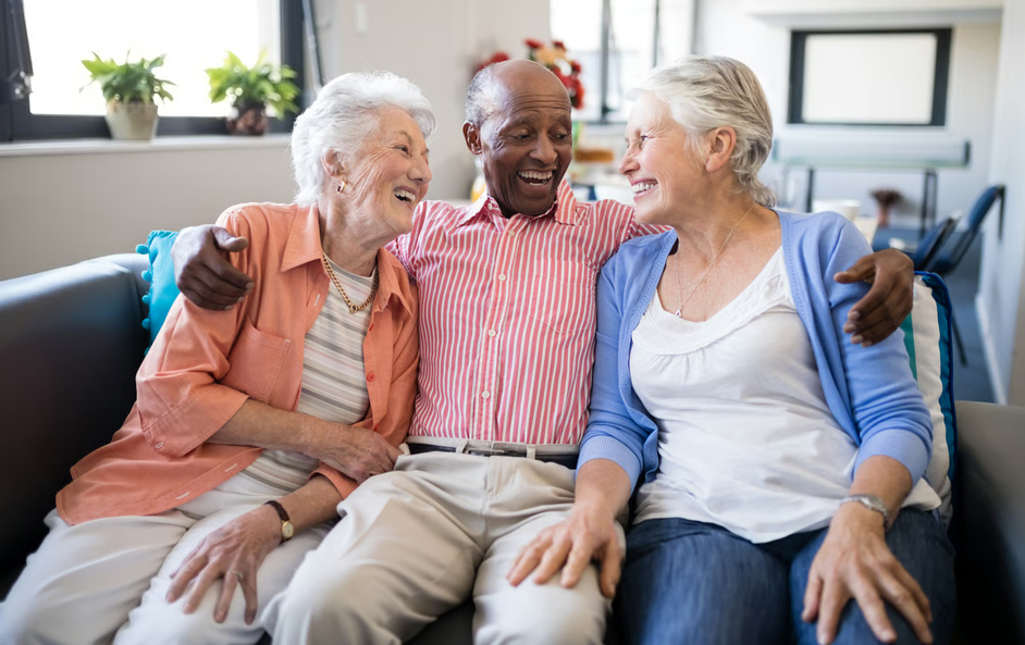 An elderly male veteran smiling happily while sitting on a couch flanked by two supportive women during hospice care.