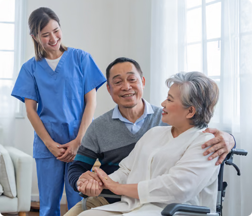 Caregiver in blue scrubs assisting a smiling elderly couple during an in-home senior care visit